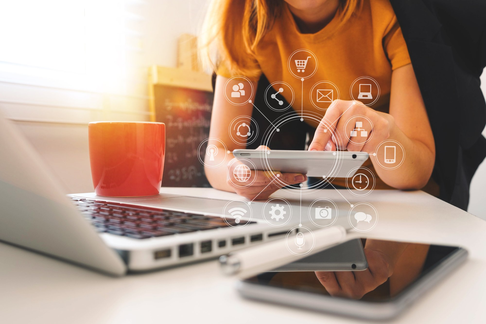 Woman working on tablet with laptop and phone on the table. Icons related to local marketing and franchise pop up